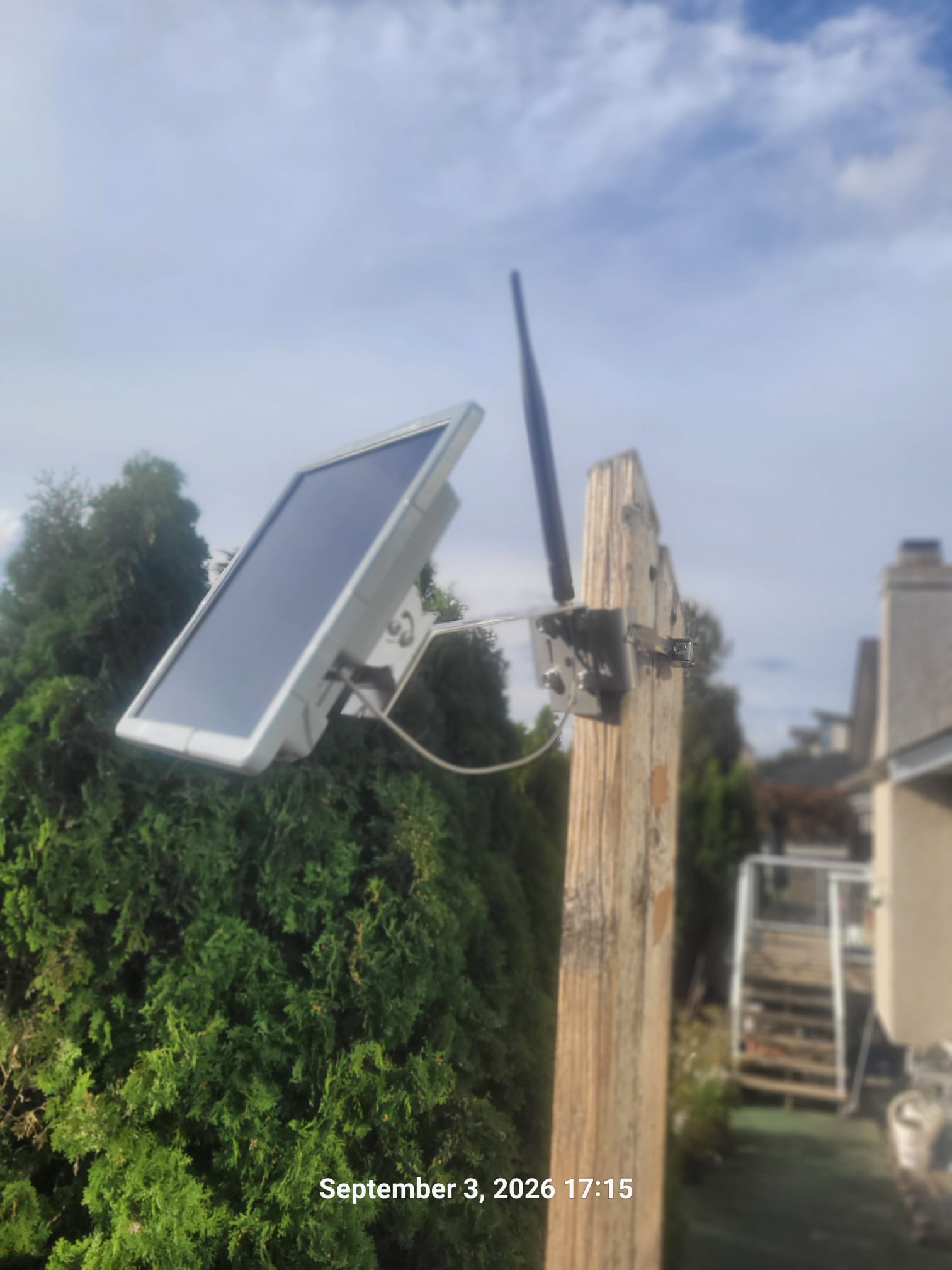 VA7REF solar-powered MeshCore repeater with a solar panel and vertical antenna mounted on a wooden post